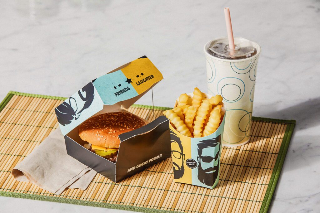 Vue montrant un hamburger dans une coquille à base de fibres, un emballage pour frites et des gobelets pour boissons froides dans un restaurant à service rapide