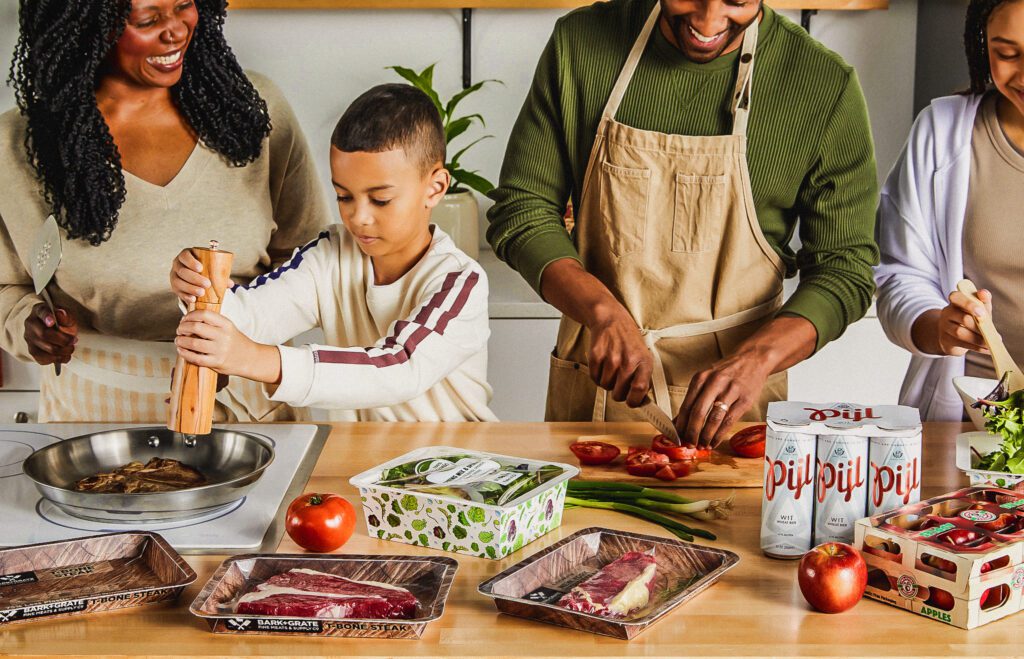 Une famille de quatre personnes cuisine en utilisant divers produits de Graphic Packaging, notamment le plateau PaperSeal, ProducePack, etc.
