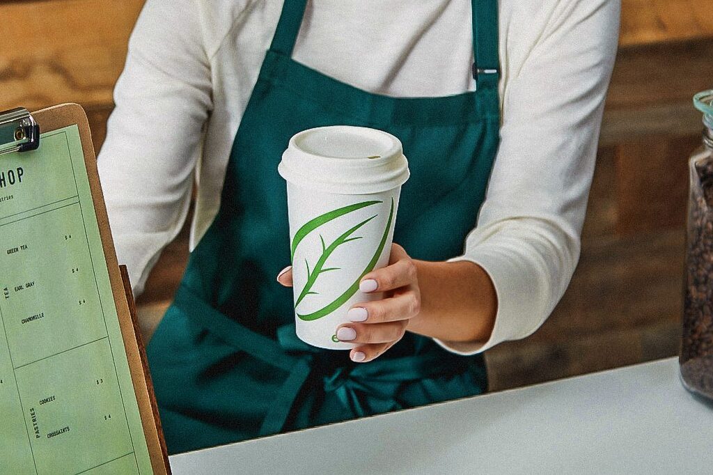 Un barista tend un café à quelqu’un en utilisant un gobelet pour boisson chaude ecotainer de Graphic Packaging